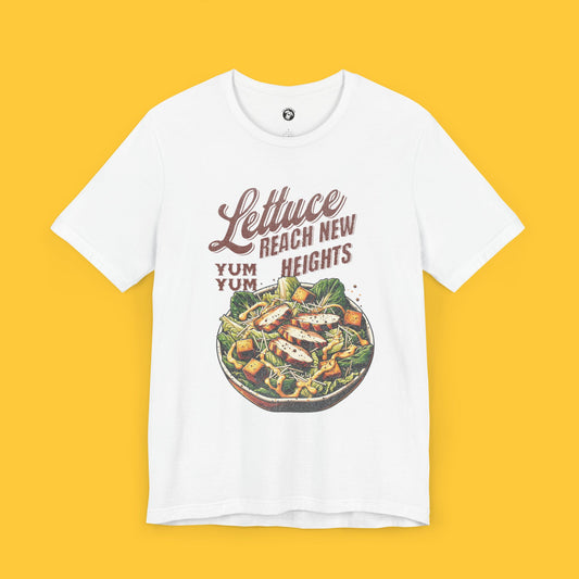 T-shirt featuring a graphic of a Caesar salad bowl with the quote "Lettuce Reach New Heights" in vintage-inspired typography.