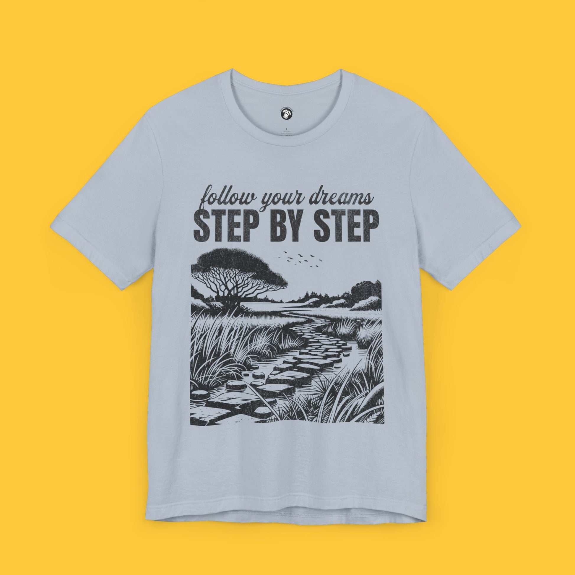 T-shirt with a minimalist landscape silhouette and the quote "Follow your dreams, step by step" in bold text.