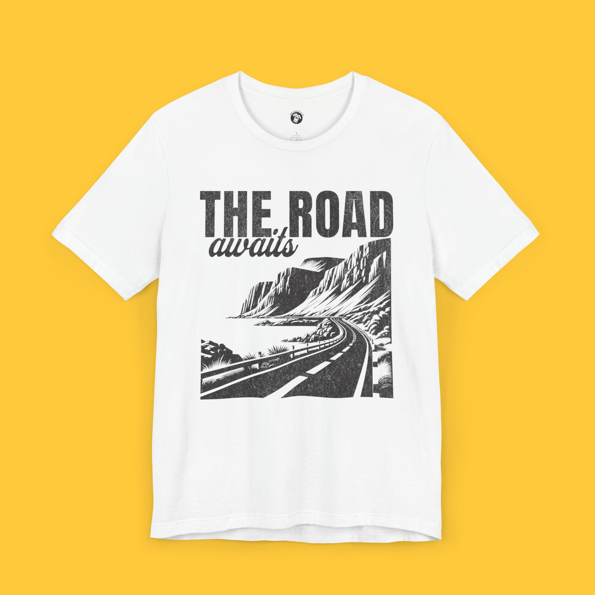 T-shirt featuring a landscape silhouette of a winding road along a rugged coastline with the quote "The Road Awaits."